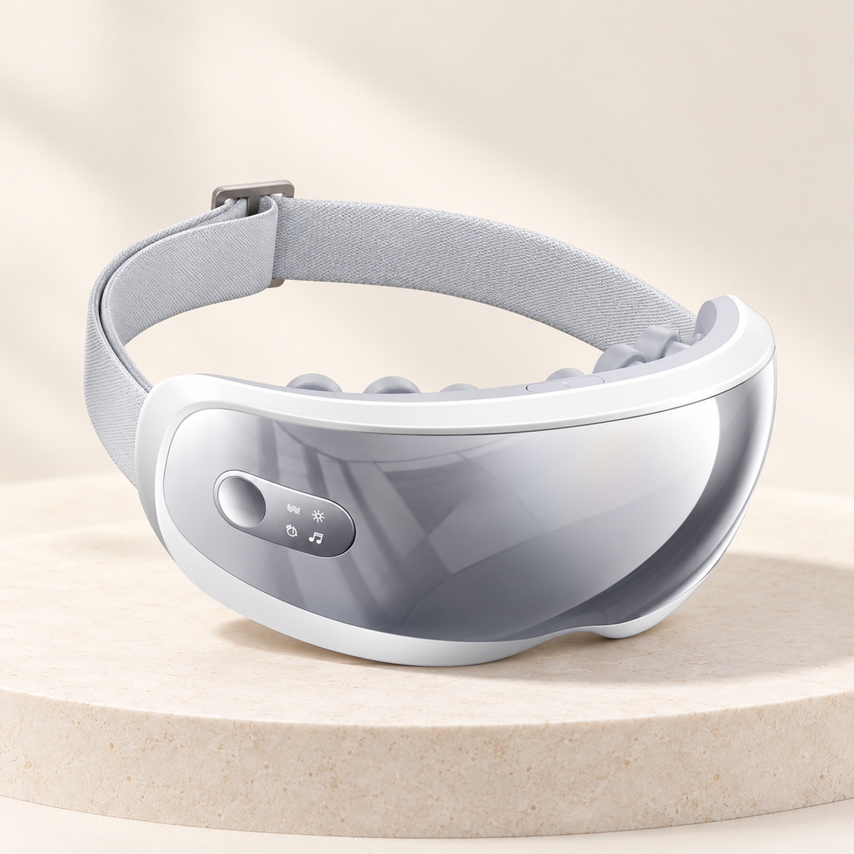 White heated eye massager with a gray front and adjustable strap on a cream display pedestal